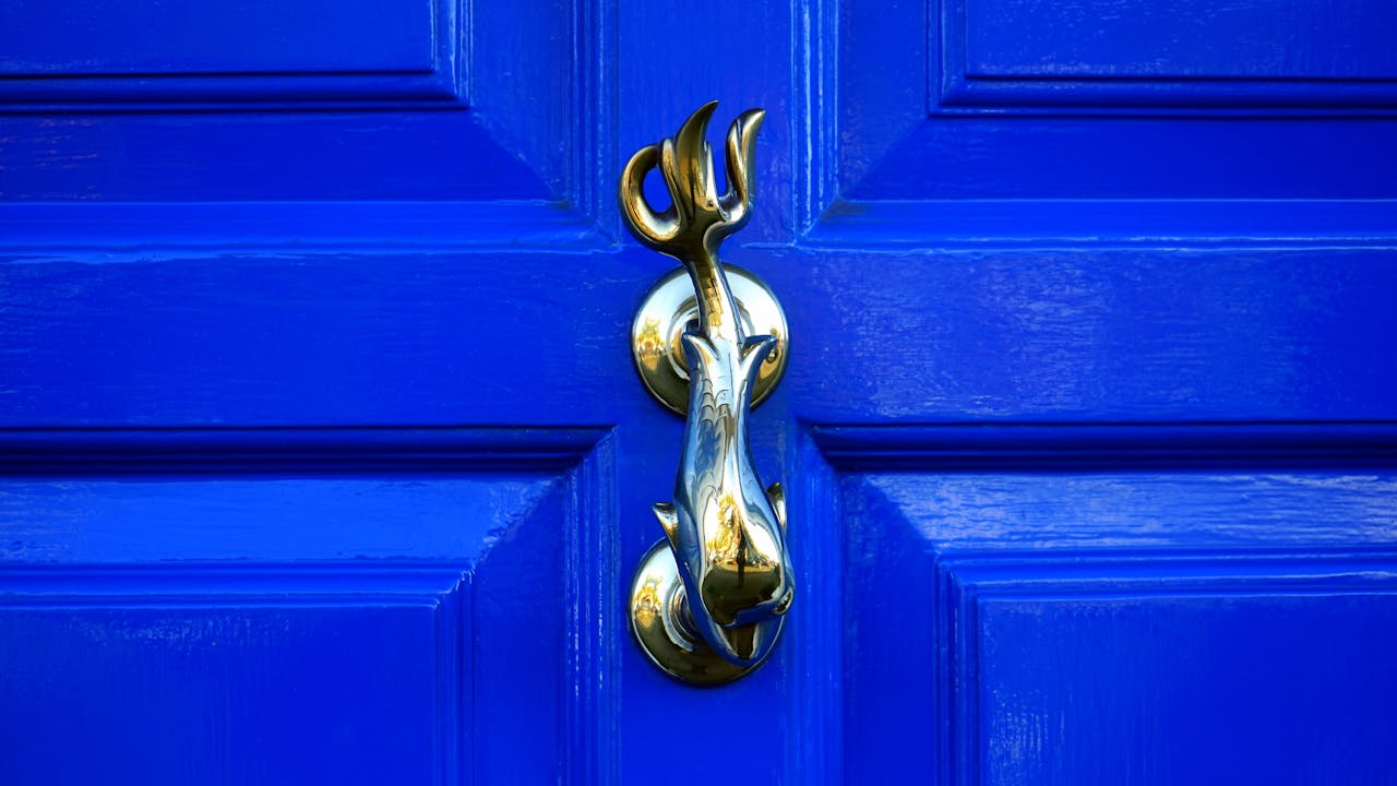 Close-up of a vintage golden door knocker on a vibrant blue wooden door in Buckinghamshire, England.