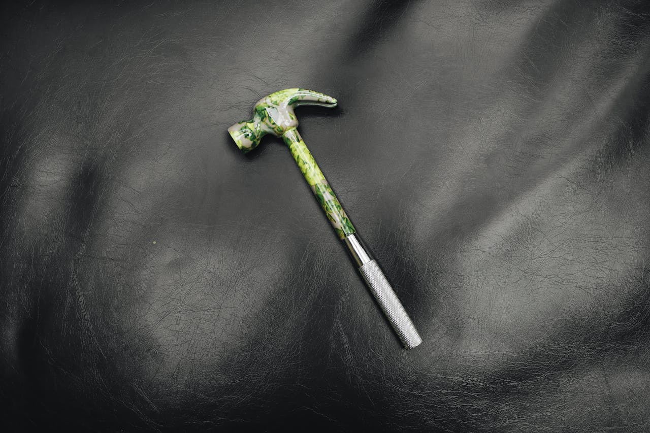 Unique hammer with a colorful handle on textured black leather surface.